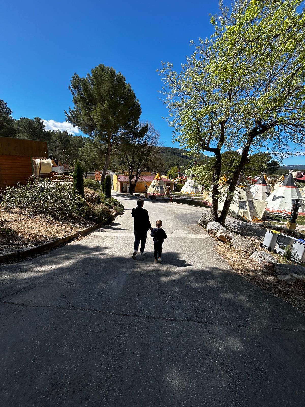 Maman et enfant marchant main dans la main vers les tipis du camping OK Corral